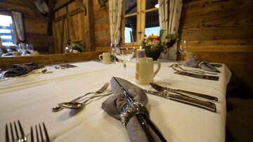 A stylishly laid table in a wood-paneled room. The table setting includes cutlery, glasses, and a flower vase.