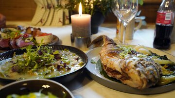 A decorated table with delicious food. Grilled fish is next to a bowl of vegetables and a bowl of salad.