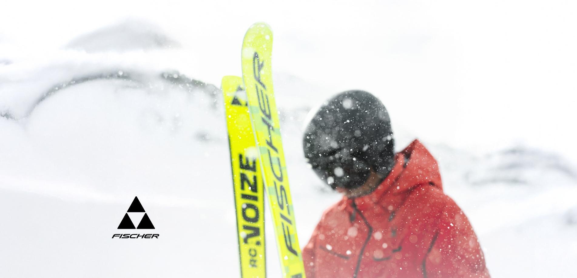 A skier is standing in the snow with yellow skis. The surroundings are wintry and covered with snow.