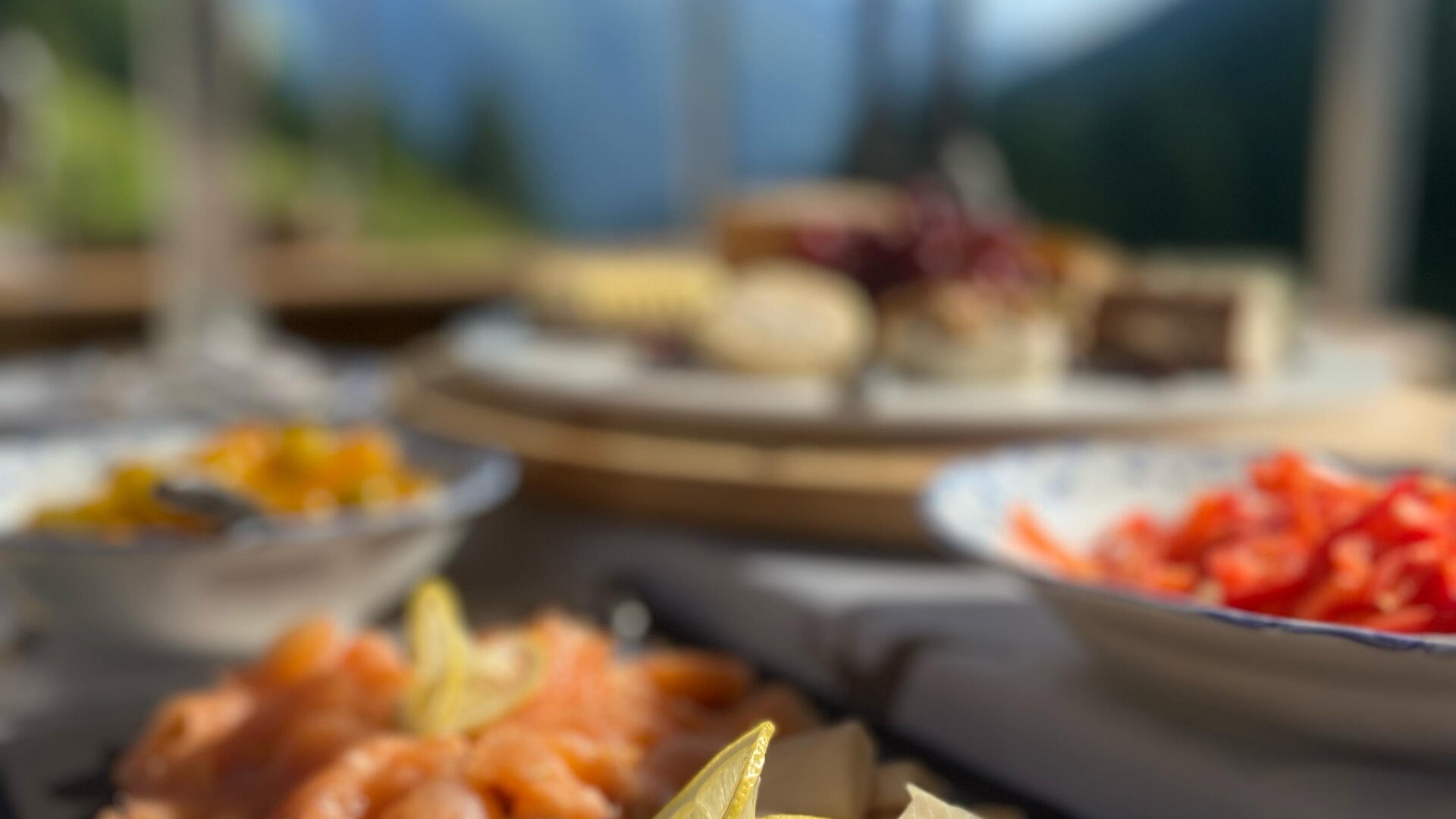 Eine ansprechend angerichtete Auswahl an Fischplatten, garniert mit Zitrone. Im Hintergrund sind weitere Speisen und eine schöne Landschaft zu sehen.