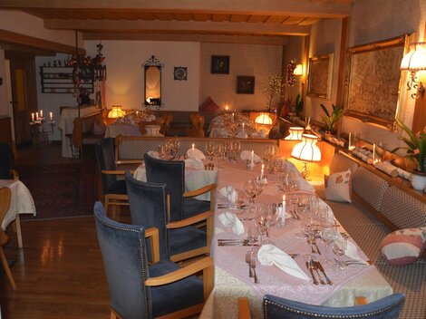A cozy restaurant with a long, covered table and warm light. The decor is inviting and friendly.