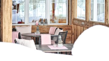 Ein gemütliches Restaurant mit Holzwänden und großen Fenstern. Die Tische sind stilvoll mit rosa Tischdecken und Dekorationen gedeckt.