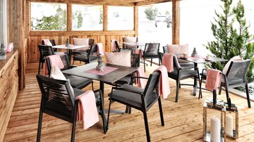 Ein stilvolles Café mit Holzdekor und gemütlichen Tischen. Die Terrasse ist mit bequemen Stühlen und sanften Textilien ausgestattet.