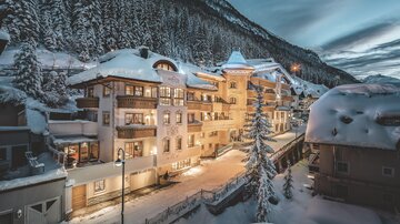 Eine malerische Winterlandschaft mit schneebedeckten Häusern und Bergen. Die warmen Lichter der Gebäude leuchten in der Abenddämmerung.