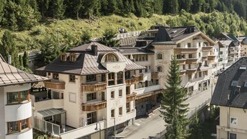 Eine malerische alpine Landschaft mit modernen Gebäuden. Im Hintergrund sind grüne Hügel und Wälder zu sehen.