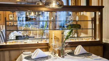 Ein elegantes Restaurant mit einer schön gedeckten Tafel. Die Einrichtung ist modern und einladend, mit Glas- und Holzelementen.