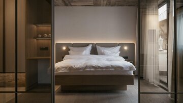 Ein modernes Schlafzimmer mit einem großen Doppelbett und sanfter Beleuchtung. Die Wände sind in neutralen Tönen gehalten, und es gibt großzügige Fenster, die natürlichen Licht hereinlassen.