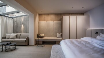 Ein modernes Zimmer mit einem hellen Schlafzimmer und einem gemütlichen Sitzbereich. Große Fenster sorgen für viel Tageslicht und eine einladende Atmosphäre.