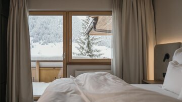 Ein gemütliches Schlafzimmer mit Blick auf eine verschneite Landschaft. Große Fenster lassen viel Licht herein und zeigen winterliche Berge und Bäume.