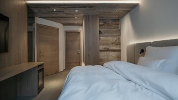 Ein modernes Schlafzimmer mit einem großen Bett und einem Holzdesign. Die Wände sind hell und die Beleuchtung sorgt für eine gemütliche Atmosphäre.