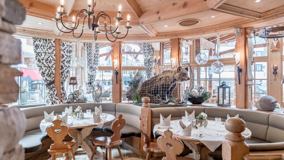 Ein gemütliches Restaurant mit Holzdekor und einer Bärenfigur im Hintergrund. Die Tische sind hübsch gedeckt und schaffen eine einladende Atmosphäre.