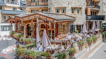 Ein gemütliches Restaurant mit Holzveranda und Terrassenplätzen. Viele Gäste genießen die Atmosphäre im Freien.