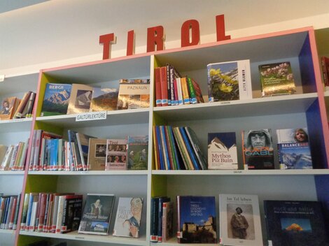 A bookshelf with many different titles that displays the word "TIROL" above it. The books cover various topics and genres.