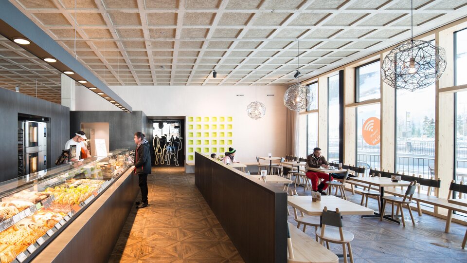 Ein modernes Café mit großen Fenstern, viel Tageslicht und einem eleganten Interieur. Die Theke ist mit verschiedenen Speisen und Getränken dekoriert. | © MPREIS Warenvertriebs GmbH