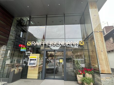 Entrance to the Raiffeisenbank with modern architecture. A cash machine and plants can be seen on the facade.