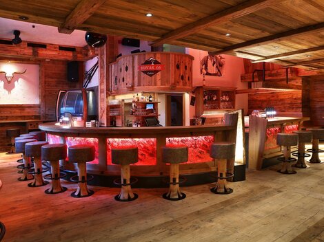 A cozy bar with wooden paneling and round stools. The lighting creates an inviting atmosphere.