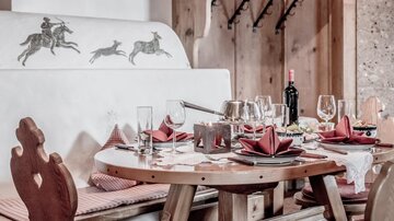 Ein liebevoll gedeckter Tisch in einem gemütlichen Restaurant. Hinter dem Tisch zeigt eine dekorative Wandmalerei verschiedene Reiter.