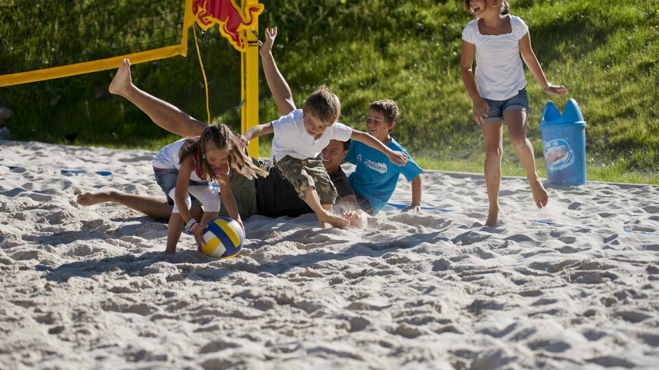 Children are playing volleyball on the beach. They are having fun in the sand and enjoying the sun.