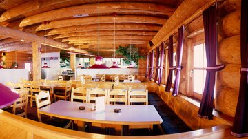 Ein gemütliches Restaurant mit Holzdecke und vielen Tischen. Die Einrichtung hat eine warme, einladende Atmosphäre.
