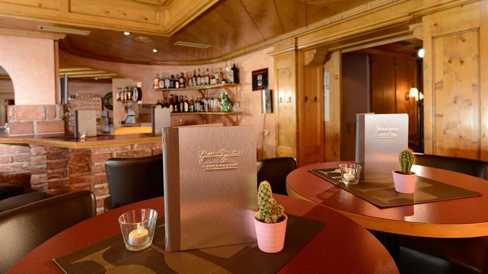 A cozy restaurant with wooden walls and an inviting bar. Menu cards and small potted plants are on the tables.