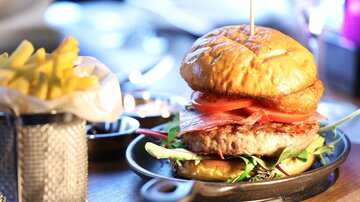 A delicious burger with fresh tomatoes and lettuce on a plate. Next to it is a portion of fries.