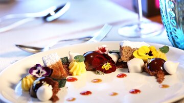 An artfully arranged dessert plate with various sweets, edible flowers, and colorful sauces. The presentation is elegant and appealing.