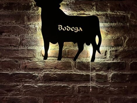 Eine stilisierte Kuhsilhouette an einer Backsteinwand. Darunter steht „Bodega“ in geschwungener Schrift.