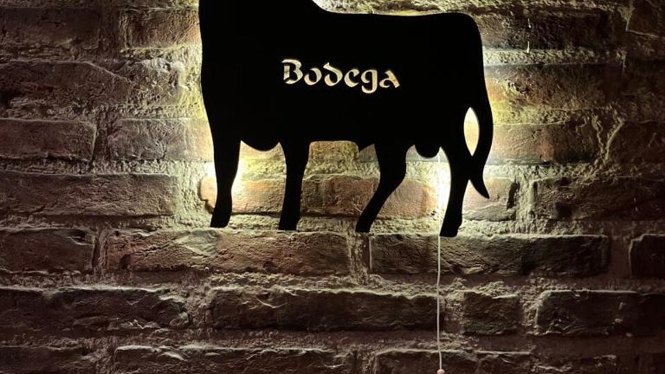 Eine stilisierte Kuhsilhouette an einer Backsteinwand. Darunter steht „Bodega“ in geschwungener Schrift.