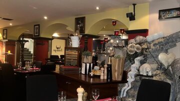 Ein stilvolles Restaurant mit dunklen Tischen und schwarzen Stühlen. Die Tische sind mit roten Servietten und Gläsern gedeckt, und die Wände sind geschmackvoll dekoriert.