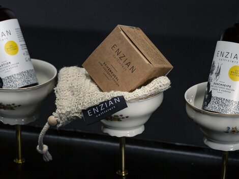 Three stylish products in elegant bowls. The bottles contain care products with a gift tag from ENZIAN.
