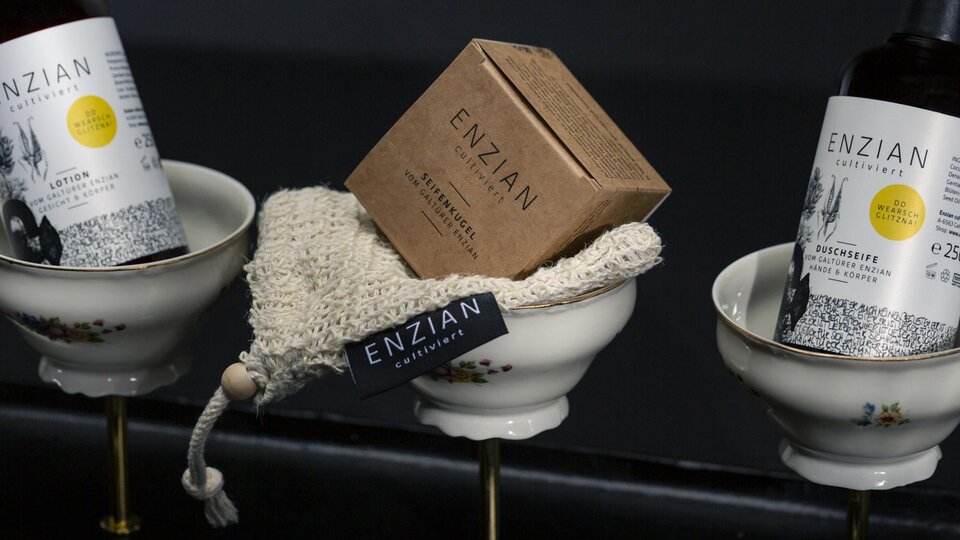 Three stylish products in elegant bowls. The bottles contain care products with a gift tag from ENZIAN.