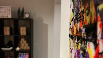A colorful wall hanging with an artistic motif is hanging on the wall. In the background, shelves with various objects can be seen.