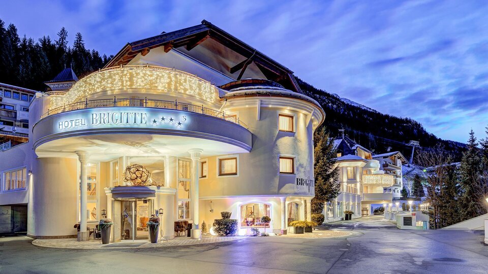 Ein elegantes Hotelgebäude mit schöner Beleuchtung. Die Umgebung ist von Bergen umgeben und der Himmel zeigt sanfte Farben des Abenddämmerungs.