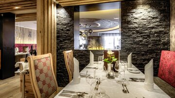 Ein elegantes Restaurant mit einem schön gedeckten Tisch und stilvollem Interieur. Im Hintergrund befindet sich ein moderner Kamin und dekorative Elemente.