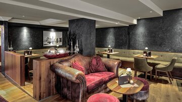 Ein gemütlicher Innenraum mit einem großen Ledersofa und Holzdetails. Die Atmosphäre ist warm und einladend, ideal für entspannte Treffen.
