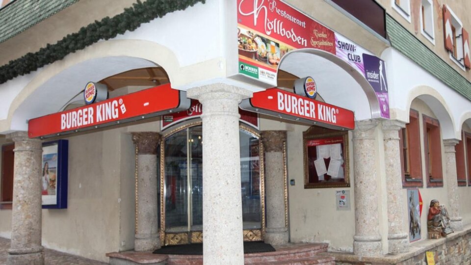 Ein Burger King Restaurant mit auffälligem roten Schild. Das Gebäude hat Säulen und ist in einer urbanen Umgebung.