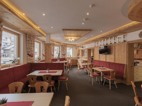 A cozy restaurant with wood decor and red upholstered benches. There are tables with space for guests and large windows that let in natural light.