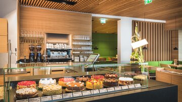 Ein modernes Café mit einer Auswahl an bunten Torten und einem eleganten, hellen Interieur. Die Vitrine zeigt verschiedene Kuchen, die zum Verweilen einladen.