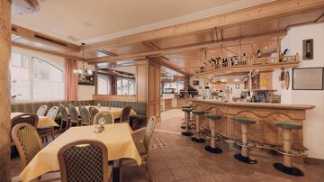Ein gemütliches Restaurant mit Holzelementen und einer freundlichen Atmosphäre. Die Einrichtung ist elegant und einladend, mit Tischen und Barhockern.