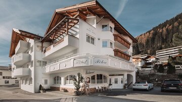 Ein modernes Hotelgebäude mit einem charakteristischen Dach und einer einladenden Fassade. Es liegt in einer malerischen Berglandschaft.