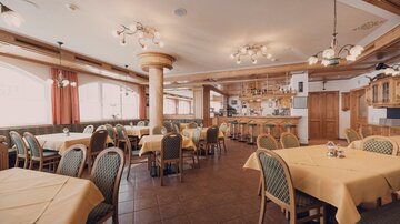 Ein gemütliches Restaurant mit Tischen in hellem Gelb und Stühlen aus Holz. Die Einrichtung ist rustikal und einladend, mit großen Fenstern, die viel Licht hereinzulassen.