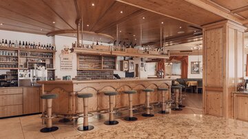 Eine gemütliche Bar mit Holzdesign und Hockern. Im Hintergrund sind Regale mit Getränken zu sehen.