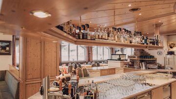 Eine elegante Bar mit Holzelementen und einer umfangreichen Auswahl an Spirituosen. Gläser sind ordentlich auf dem Thekenbereich angerichtet.