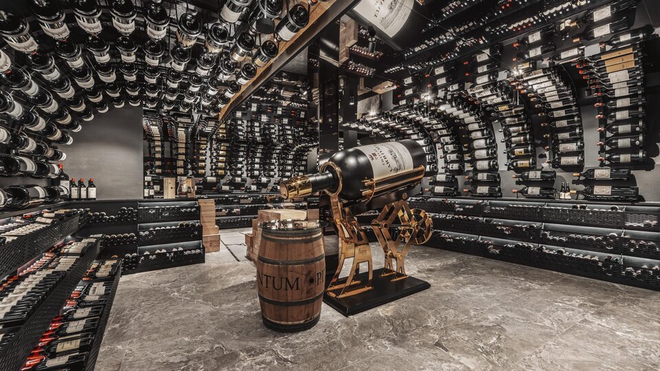Ein eleganter Weinkeller mit vielen Regalen voller Weinflaschen. In der Mitte steht ein Fass und eine dekorative Weinpressmaschine.
