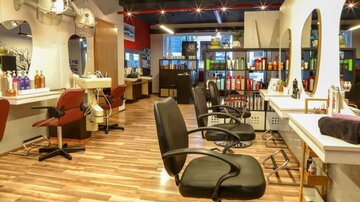Ein moderner Friseursalon mit mehreren Stylistensesseln und gut sortierten Regalen. Die Wände sind hell und die Einrichtung wirkt einladend und gemütlich.
