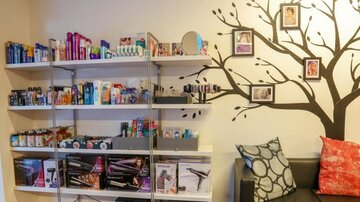 Ein gemütlicher Raum mit Regalen voller Pflegeprodukte und Styling-Werkzeuge. An der Wand befindet sich ein Baum-Motiv mit Fotos.