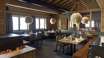 Ein modernes Restaurant mit Holzdekor und gemütlicher Atmosphäre. Die Tische sind elegant eingedeckt und große Fenster bieten einen Blick nach draußen.