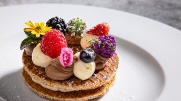 Ein kunstvolles Dessert mit knusprigen Waffeln, Schokoladencreme und bunten Beeren. Frische essbare Blumen verleihen dem Gericht einen besonderen Akzent.