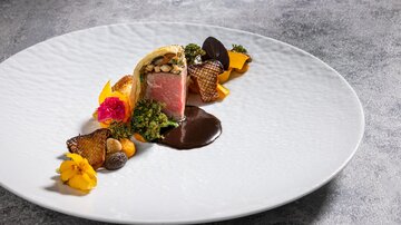 Ein kunstvoll angerichteter Teller mit Fleisch und bunten Beilagen. Die Präsentation enthält essbare Blumen und verschiedene Texturen.