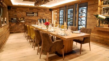 Ein eleganter Essraum mit einem langen Holztisch und gepolsterten Stühlen. Die Wände sind aus Holz, und der Raum hat eine gemütliche Atmosphäre.